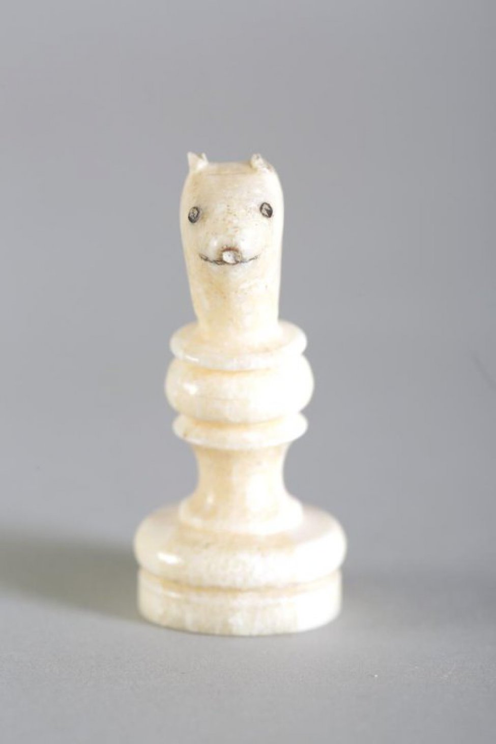 Шахматная фигура белого цвета в виде невысокой профилированной балясины вверху заканчивается головой песца с  отбитыми  ушами. На голове  неглубокой резьбой (процарапыванием) с черной тонировкой обозначены  маленькие круглые глаза, линия рта и кончик носа. Вся фигура выполнена из одного куска бивня.