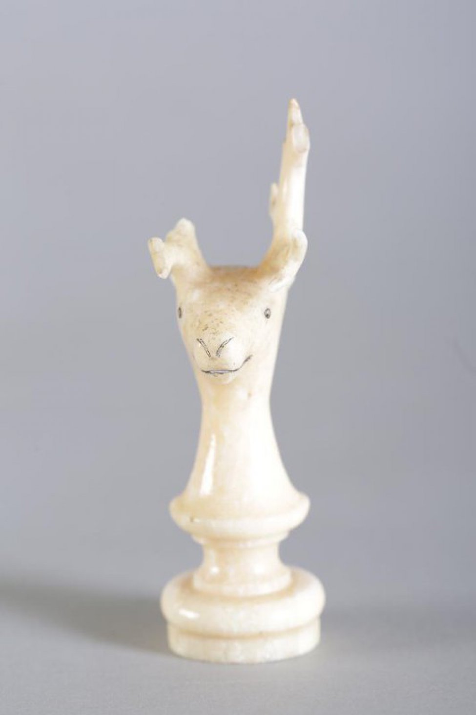 Шахматная фигура белого цвета в виде невысокой балясины, вверху заканчивающаяся головой рогатого оленя.  Маленькие круглые глаза, линия рта и кончик носа  обозначены неглубокой резьбой (процарапыванием) с черной тонировкой. Вся фигура выполнена из одного куска бивня.